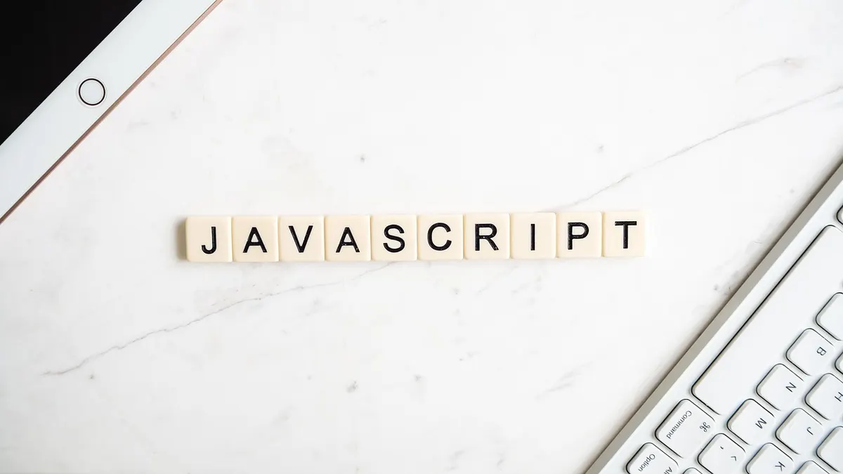 The word JavaScript spelled in tiles next to a keyboard, representing Angular vs React comparison