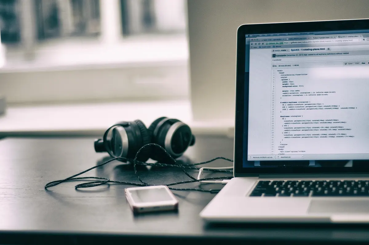 Laptop displaying source code on GitHub next to headphones on a developer's desk