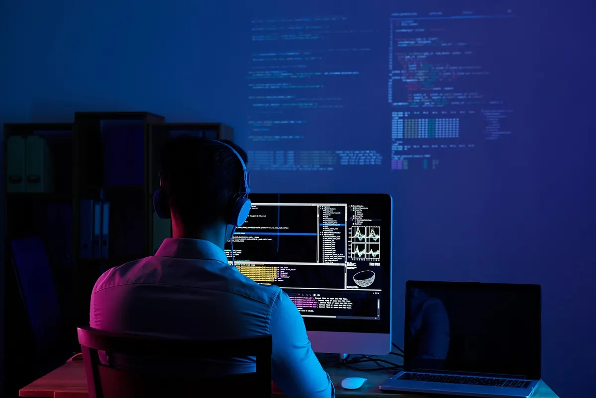 Software developer analyzing website performance code on dual monitors at night
